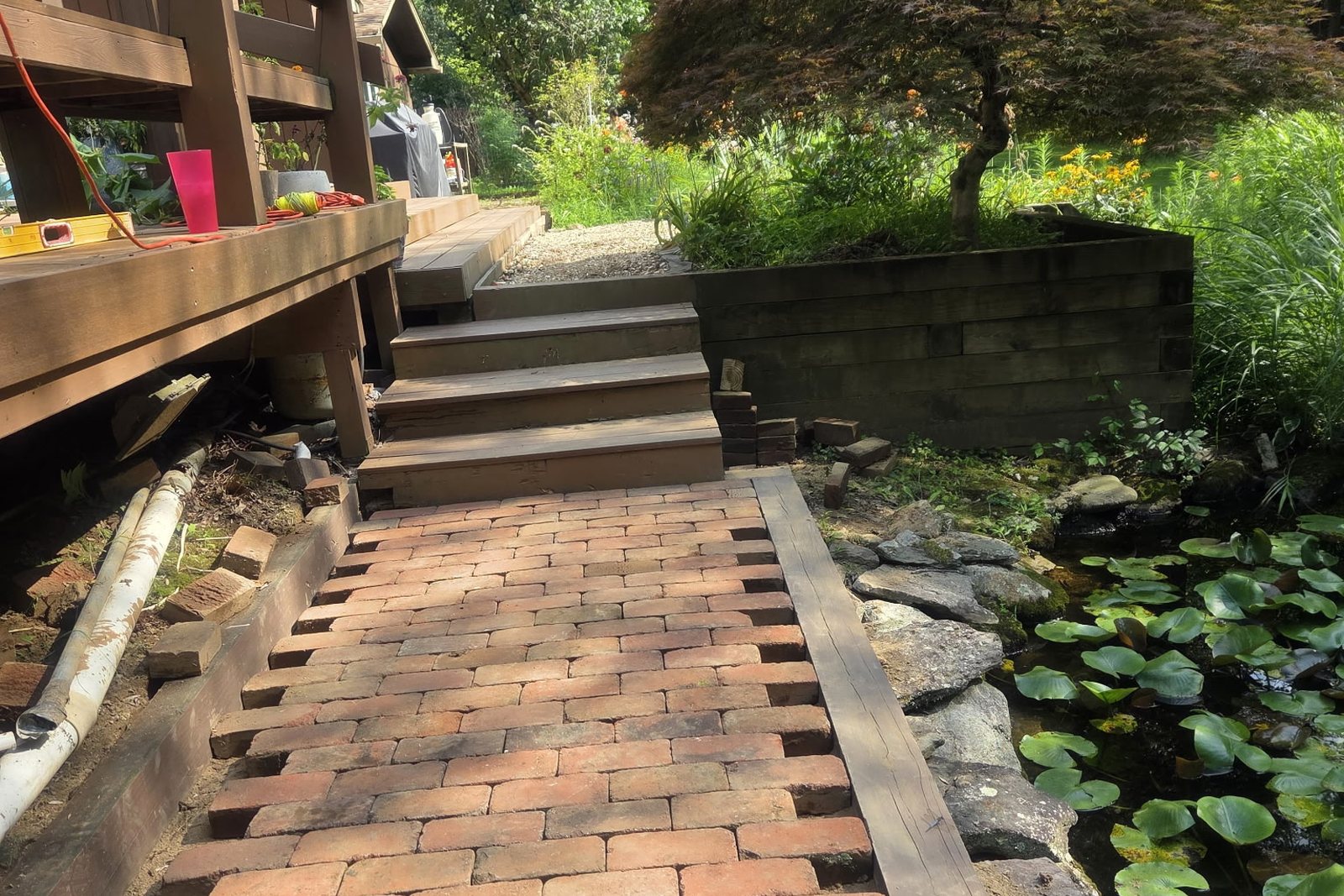 A brick paver patio being laid beside a garden pond